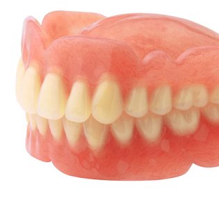 An up-close view of a top and bottom denture made from a gum-colored base and artificial teeth