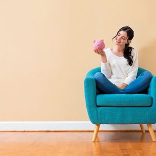 Woman smiling at her piggy bank while sitting on a chair