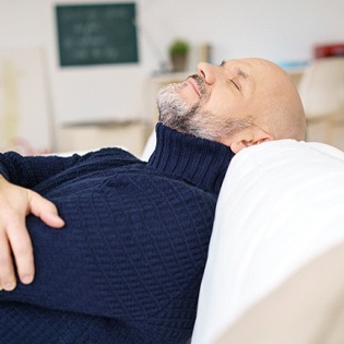 A man wearing a navy sweater and relaxing against the back of the couch after his dental appointment