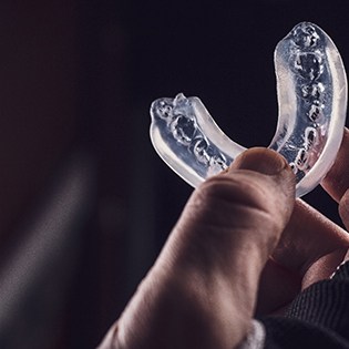 Man holding clear mouthguard against black background