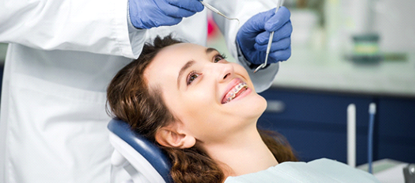 A young woman wearing traditional braces in Tappan and smiling as the orthodontist prepares to check her teeth