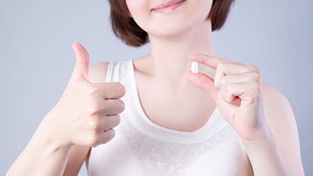 A smiling woman holding an extracted wisdom tooth while giving a thumbs up